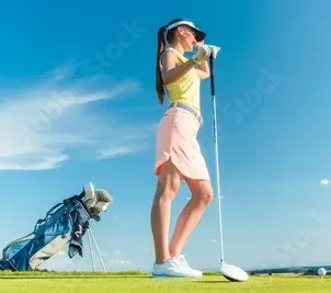 Golfspielerin steht am Abschlagspunkt, stützt sich auf ihrem Driver ab; Standbag steht neben ihr
