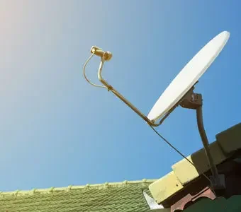Satellitenschüssel auf Hausdach zeigt in den blauen Himmel