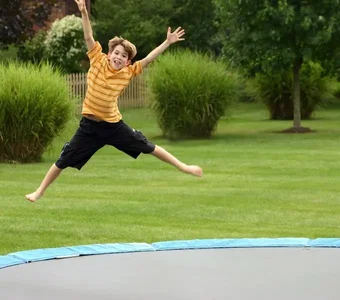 Ein Junge springt auf einem Gartentrampolin und streckt seine Arme und Beine in der Luft von sich