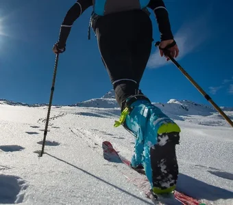 Frau mit Touren-Ski und Skistöcken beim Aufstieg