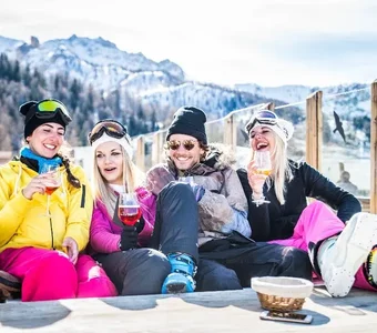 Eine Vierergruppe mit in Snowboardoutfits sitzt draußen auf einer Couch am Tisch