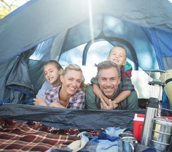 Familie mit zwei Kindern schaut lächelnd aus dem Zelt heraus