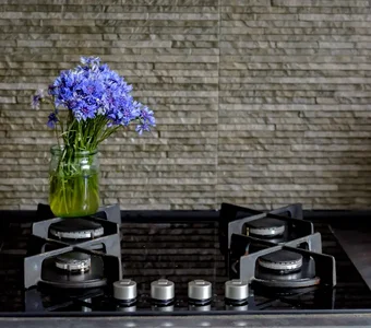 Neben einem modernen Gasherd mit vier Kochplatten befindet sich ein Blumenstrauß aus blauen Kornblumen