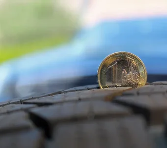 Nahaufnahme einer 1-Euro-Münze, die in einem Autoreifenprofil steckt