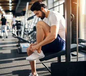 Mann schnürt Schnürsenkel von Sportschuhen im Fitnesstudio vor Training