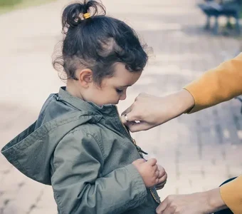 Mutter schließt den Reißerschluss der olivfarbenen Jacke ihrer Tochter