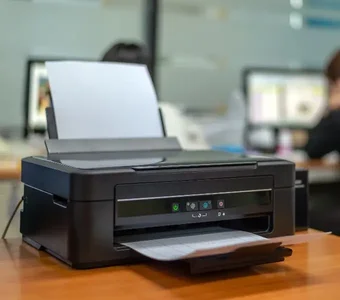Schwarzer Tintenstrahldrucker mit Papier steht auf einem Tisch in einem Büro
