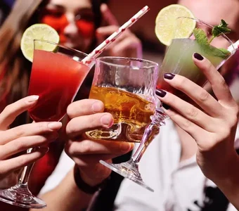 Drei Personen stoßen mit verschiedenen Cocktails und Drinks in einer Bar an