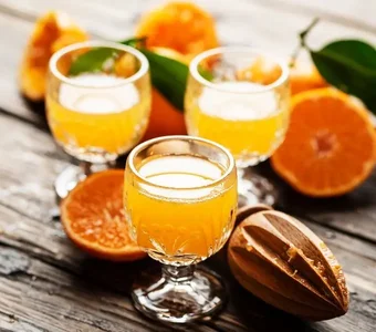 Drei Digestif-Gläser mit Orangenlikör und Fruchtgarnitur stehen auf einem Holztisch