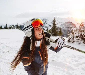 Junge Frau mit Skijacke und Skiern über der Schulter steht auf einer Piste