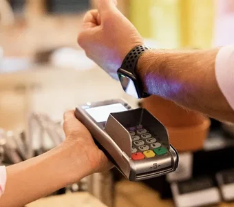 Mann bezahlt an der Kasse mit einer Smartwatch und einem Kartenlesegerät