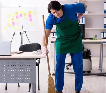 Reinigungskraft fegt im Büro und hat Rückenschmerzen