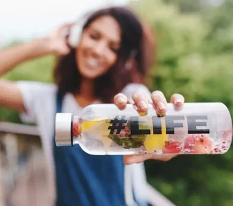 Junge Frau hält Glasflasche mit Wasser und Obst waagerecht in die Kamera