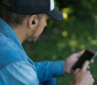 Junger Mann mit In-Ear- Kopfhörern tippt auf seinem Smartphone