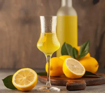 Limoncello in einem Grappa-Glas steht vor einem Brett mit Zitronen und einer gefüllten Likörflasche