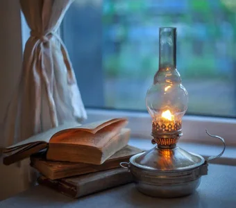 Eine antike Petroleumlampe aus Messing mit bauchigem Glaszylinder steht neben einem Stapel Bücher am Fenster