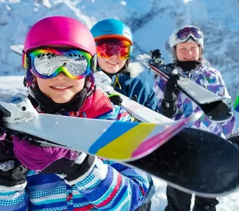 Jungen und Mädchen mit Skibrillen und Helmen tragen ihre Skier auf den Schultern