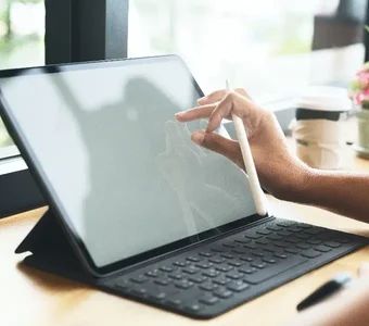 Person mit einem Smart Pen in der Hand tippt auf das Display eines Tablets mit Tastatur