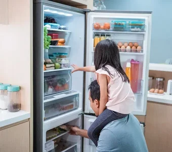 Vater mit Tochter auf den Schultern holt Lebensmittel aus dem Kühlschrank