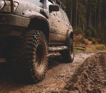 Silberfarbener Geländewagen mit Mud-Terrain-Reifen fährt auf einem matschigen Waldweg