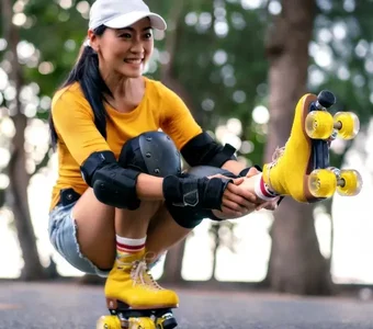 Junge Frau mit gelben Rollschuhen in der Hocke hält ihr gestrecktes Bein fest
