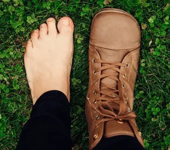 Close-up von zwei Füßen, wovon einer in einem braunen Barfußstiefel steckt