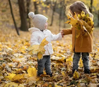 Zwei Kinder stehen im Wald und halten gelbe Blätter in der Hand