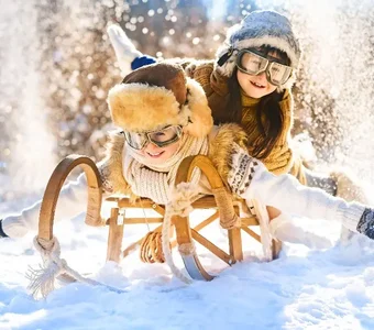 Zwei Kinder auf einem Schlitten toben durch den Schnee