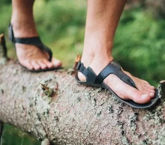 Close-up von Füßen in Barfuß-Sandalen, die über einen Baumstamm balancieren