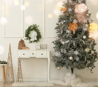 Weiß geschmückter, künstlicher Weihnachtsbaum steht neben einer weißen Anrichte mit Weihnachtsdeko