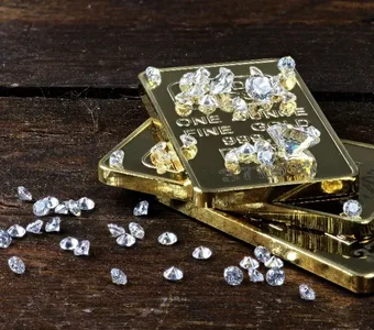 Geschliffene Diamanten liegen auf Feingold-Barren auf einem dunkelbraunen Holztisch