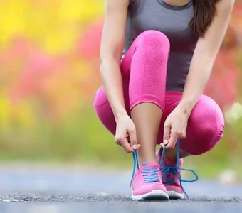 Eine Frau in Sportkleidung bindet ihre pinken Laufschuhe auf einem Asphaltboden zu
