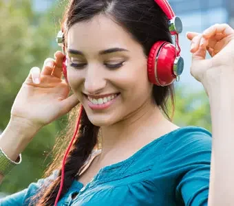 Foto einer jungen Frau, welche rote Over-Ear-Kopfhörer trägt und lächelt.
