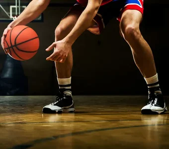 Nahaufnahme der Beine eines Basketballspielers, der zum Dribbling ansetzt. Im Fokus stehen seine Schuhe