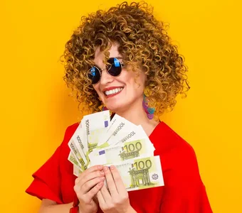 Eine sonnenbebrillte Frau mit lockiger Perücke hält ein Bündel Geldscheine in den Händen