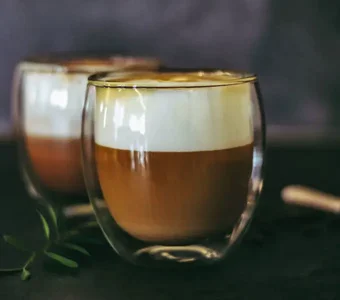 Zwei doppelwandige Gläser sind mit Kaffee und Milchschaum gefüllt