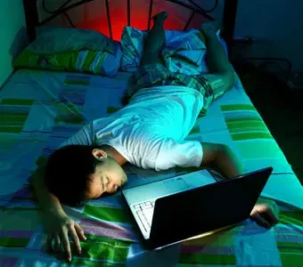 Jugendlicher liegt schlafend mit seinem Laptop auf dem Bett