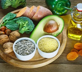 Auf einem Holztisch befinden sich Obst, Gemüse, Nüsse, Kerne, Kräuter und Öl, welche reich an Vitaminen sind