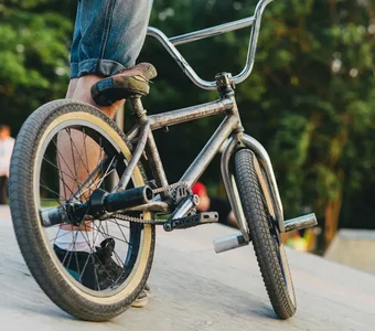 Nahaufnahme eines BMX-Rads, das in einem Bikepark von einer Person gehalten wird, im Hintergrund Bäume und Personen