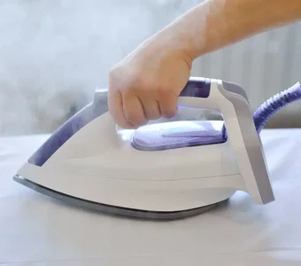 Eine Person bügelt einen weißen Stoff mit einem weißen Bügeleisen mit violetten Applikationen