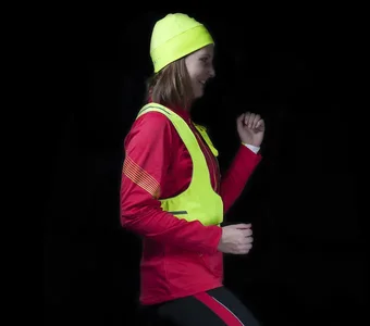 Läuferin mit Neonweste und -mütze vor schwarzem Hintergrund