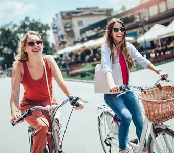 Zwei junge Frauen fahren bei guten Wetter mit ihren Citybikes durch die Stadt