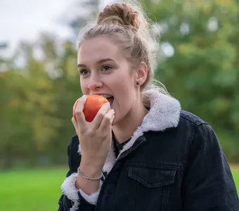 Eine junge Frau ist in der Natur unterwegs und isst einen Apfel