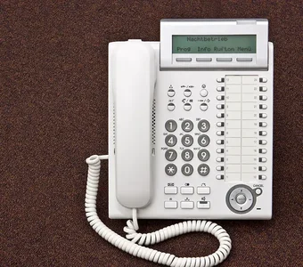 Weißes schnurgebundesnes Telefon mit Display auf braunem Untergrund