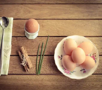 Kochlöffel, Eierbecher mit Ei und Eier auf einem Teller mit floralem Muster auf einem Holztisch