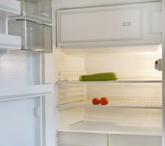 Geöffneter Kühlschrank mit Gefrierfach, in dem sich lediflich eine Zucchini und zwei Tomaten befinden
