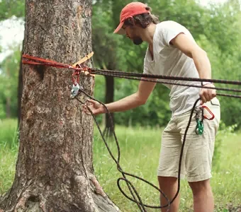 Aufnahme eines Mannes, welcher eine Slackline an einem Baum befestigt.