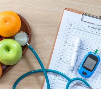 Neben einer herzförmigen Schale mit frischem Obst und Gemüse liegt ein Diabetes-Tagebuch mit einem Insulinpen und einem Blutzuckermessgerät
