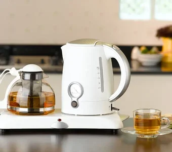 Wasserkocher und Teekanne auf einem Sockel, daneben eine Tasse Tee