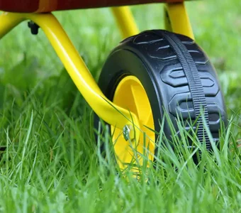 Nahaufnahme eines Rades einer gelb-roten Kinderschubkarre im Gras